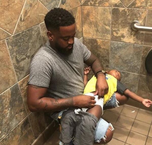 帕尔默身处佛罗里达州杰克逊维尔的一个男洗手间内。他后背倚在墙上，半蹲着给躺在自己膝盖上的儿子换尿不湿。（Instagram）