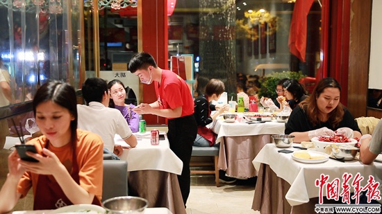 簋街胡大总店内晚10点仍座无虚席,服务员张龙为新到店客人点餐。
