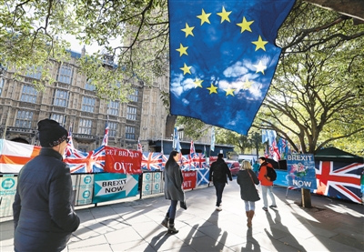 10月28日,在英国伦敦议会大厦外,行人经过欧盟旗帜、英国国旗和支持英国“脱欧”的标语牌。欧洲理事会主席图斯克当天在社交媒体推特上表示,欧盟27个成员国已同意英国提出的将“脱欧”期限推迟到2020年1月31日的申请。新华社/美联