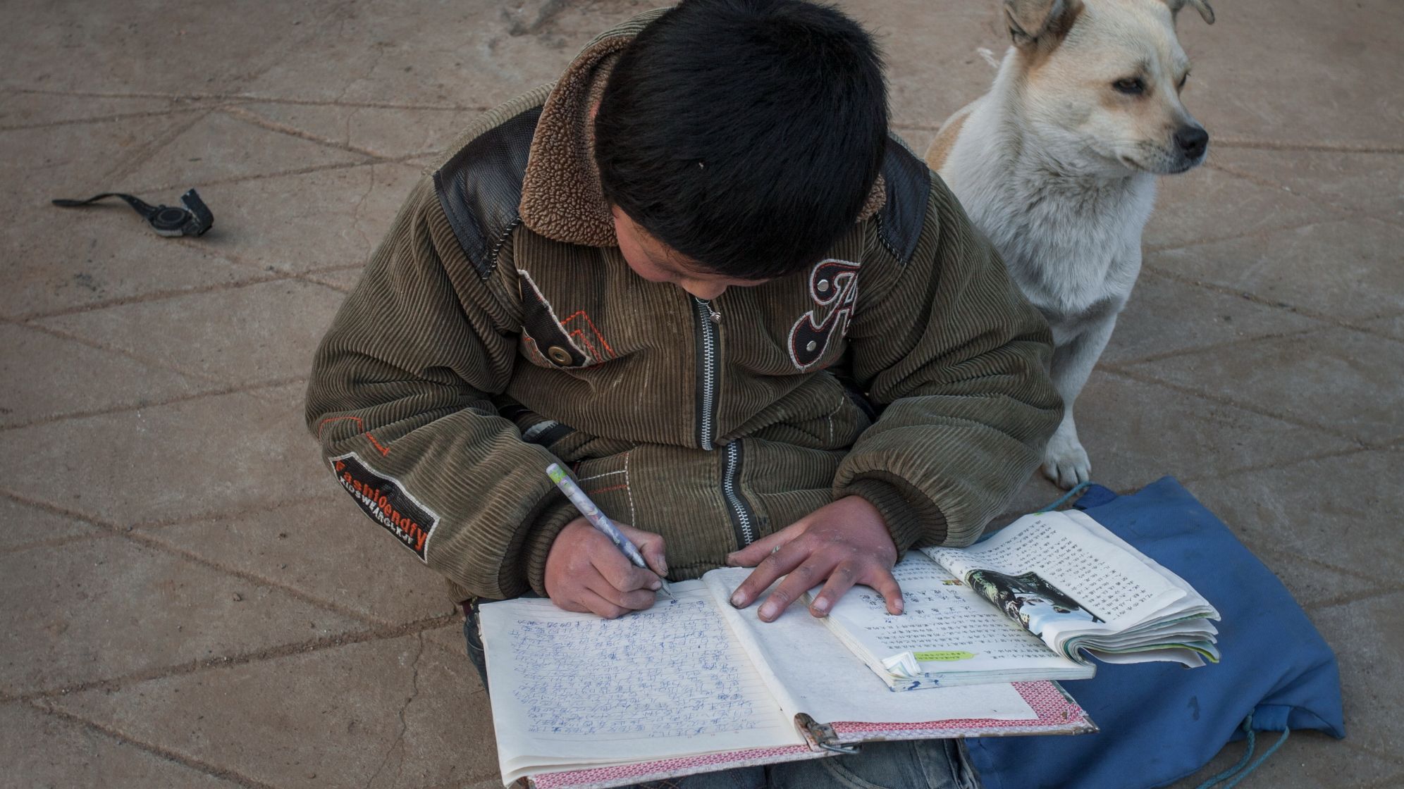 　2009年2月，小学生刘春莹在玩伴的家门口写作业。受访者供图
