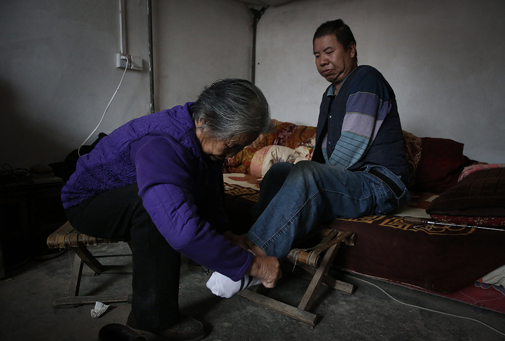 　　10月21日，河南温县招贤乡护庄村，90岁的老太太闫玉梅正帮助58岁的儿子保山起床穿衣。新京报记者 尹亚飞 摄