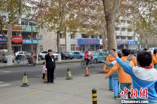 12月4日上午，在山东淄博市张店区新华学校门口，头戴贝雷帽、身材微胖的张善德站在学校门口，向前来上课的小学生鞠躬问好，并随时阻拦越过安全警戒线的车辆。　郝学娟　摄