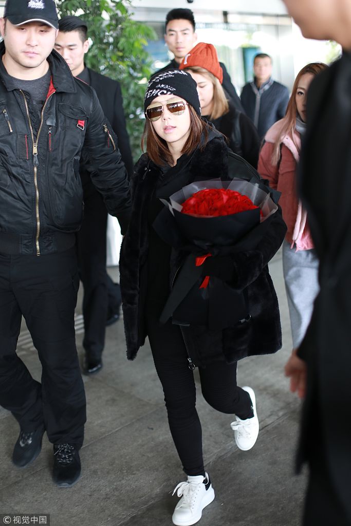 她身穿黑色皮大衣戴毛线帽酷劲十足,获保镖护驾身高差激萌显娇小,手捧