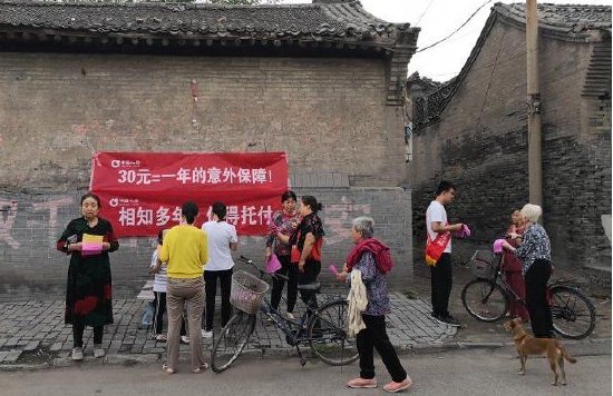图：工作人员走村入户开展小额保险政策宣传讲解